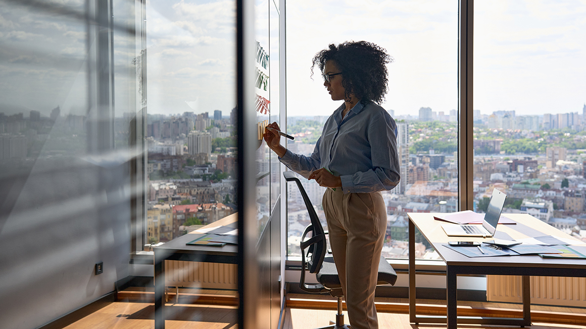 Young African american woman writing strategy ideas on sticky notes on whiteboard