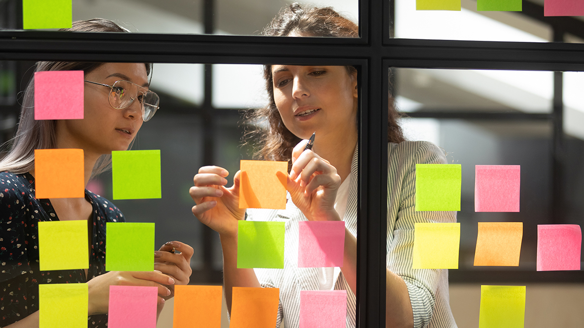 Researchers post sticky notes to a window while working on a project.