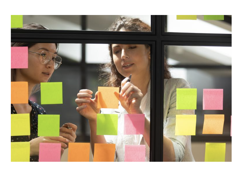 Researchers post sticky notes to a window while working on a project.