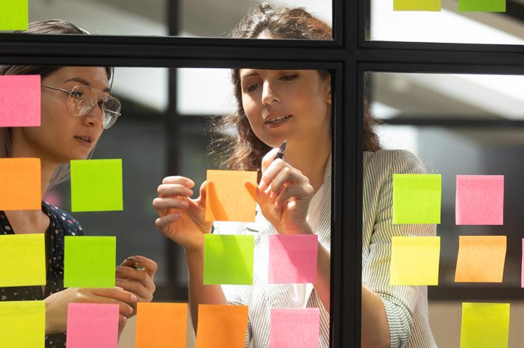 Researchers post sticky notes to a window while working on a project.